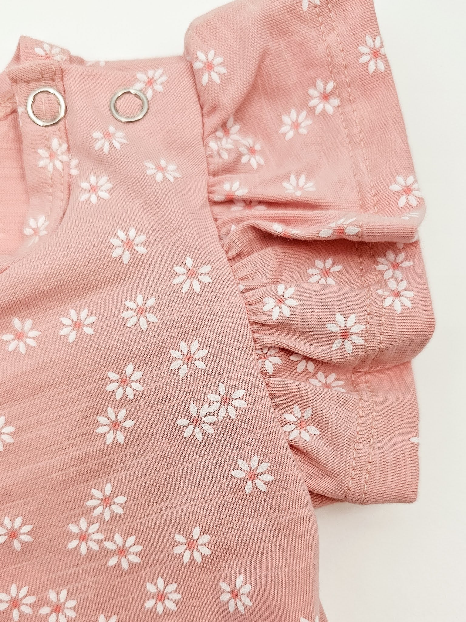 Close up of Petal Pink baby onesie with white daisies and short flutter sleeves